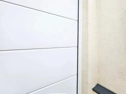 Détail en angle d'une porte de garage Hormann Renomatic blanche sur crépi beige, pose AFC Calvados.
