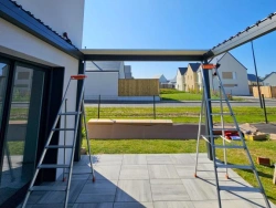 Structure de pergola Open'R anthracite en montage sur terrasse, maison moderne Normandie